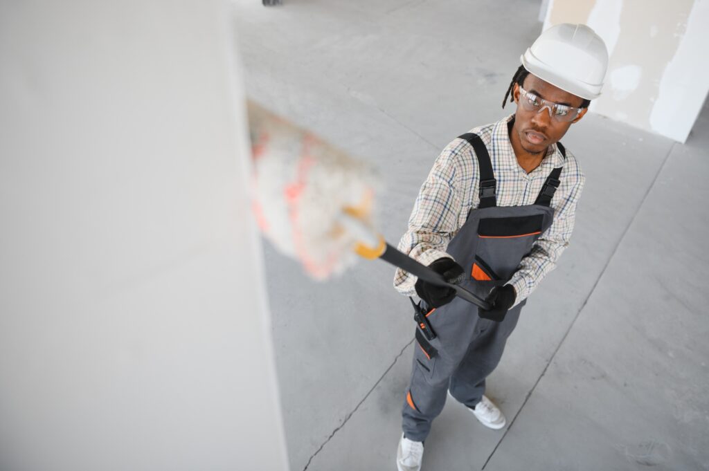 Construction worker painting walls with roller brush in building under construction